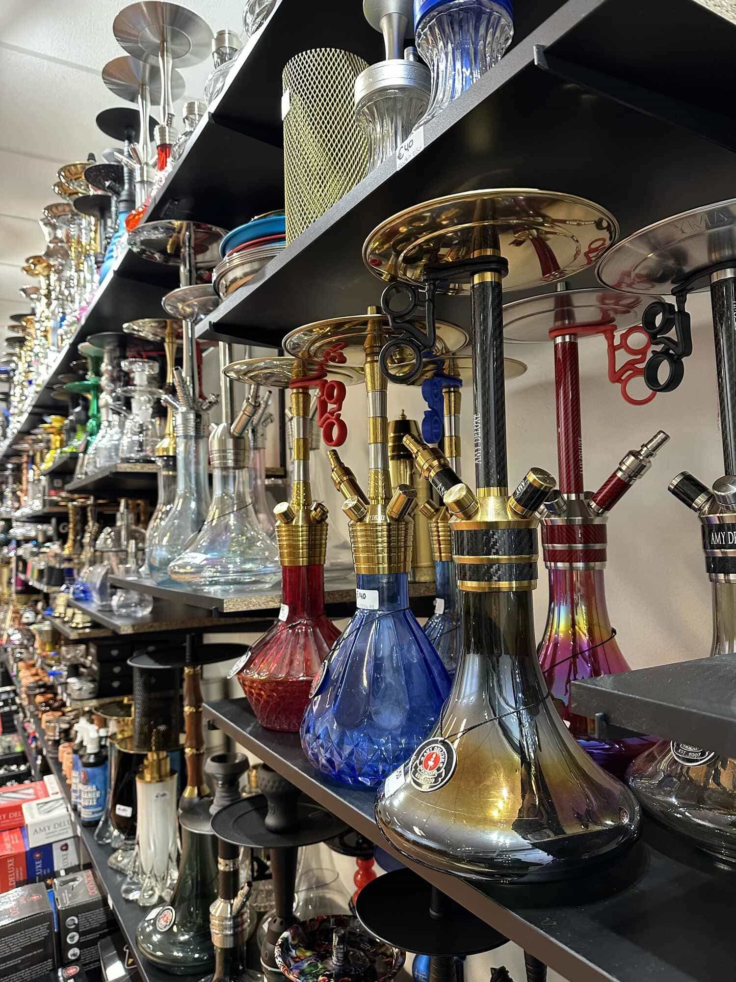 Shelves full of hookahs in the Almere shop, with glass bases in red, blue, gold and iridescent and price tags on the models.