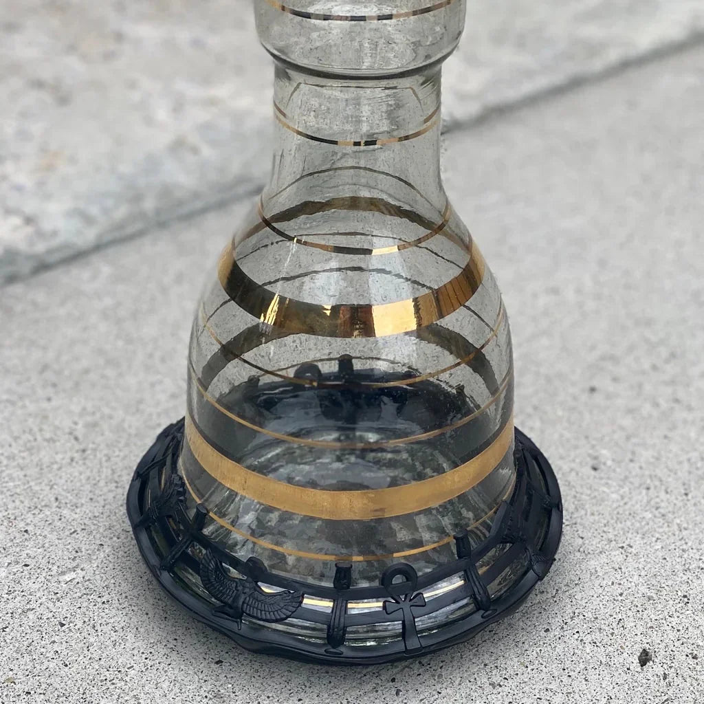 Glass hookah base with gold stripes on a concrete floor, with a black rubber protective ring around the foot.