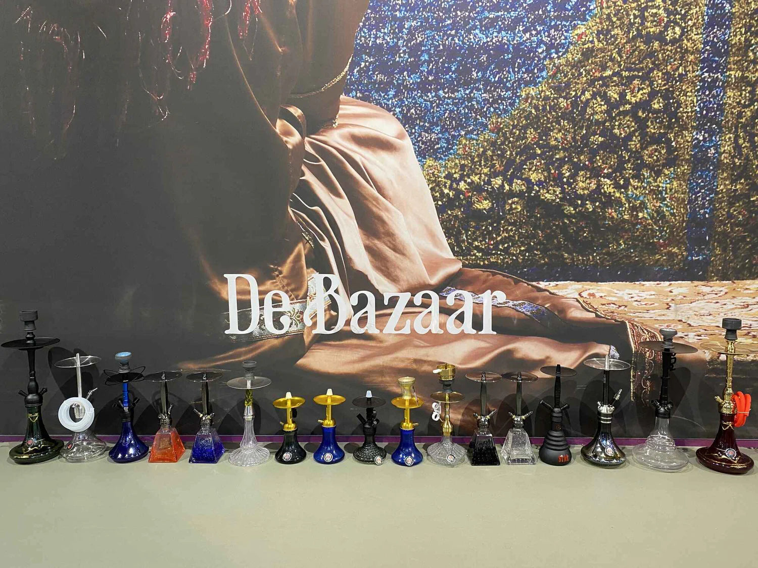 Seventeen hookahs lined up on the counter of the shop at De Bazaar in Beverwijk, in front of a large wall photo with the words De Bazaar.